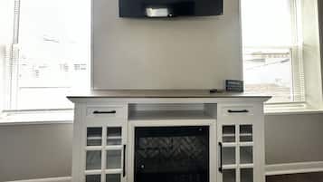 A room with a fireplace, a flat-screen TV mounted above it, and windows with blinds.