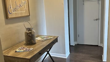 A hallway with a wooden table, a hanging light fixture, and a door with a metal rack.