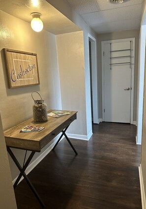 Un pasillo con una mesa de madera, una lámpara colgante y una puerta con un perchero metálico.