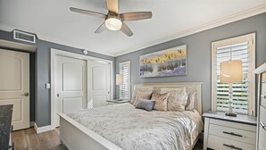 A bedroom with a bed, bedside tables, a ceiling fan, and a painting on the wall.