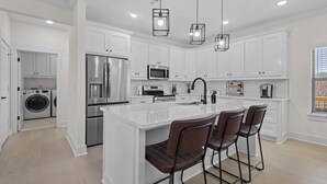 Una cocina moderna con armarios blancos, electrodomésticos de acero inoxidable y una isla central con taburetes de bar.