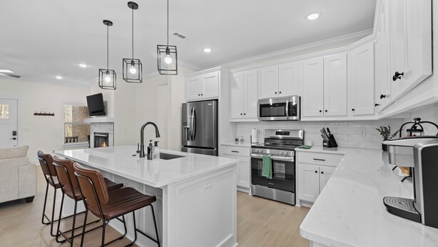 Una cocina moderna con armarios blancos, electrodomésticos de acero inoxidable y una isla central con taburetes de bar.