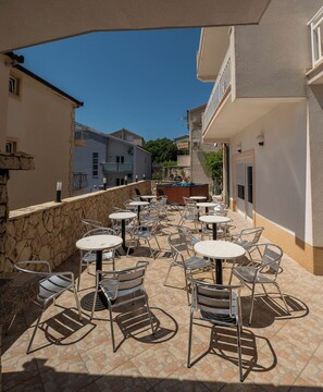 Eine Außenpatio mit mehreren runden Tischen und Stühlen, einer Steinmauer und Blick auf umliegende Gebäude.