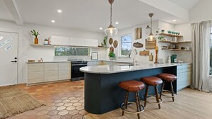 Una cocina moderna con una isla central, taburetes de bar e iluminación colgante.