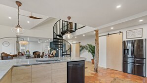 Una cocina moderna con una isla central, una escalera en espiral y un refrigerador grande.