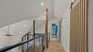 Un interior moderno con suelo de madera, baranda de vidrio y una escalera que sube a un segundo piso.