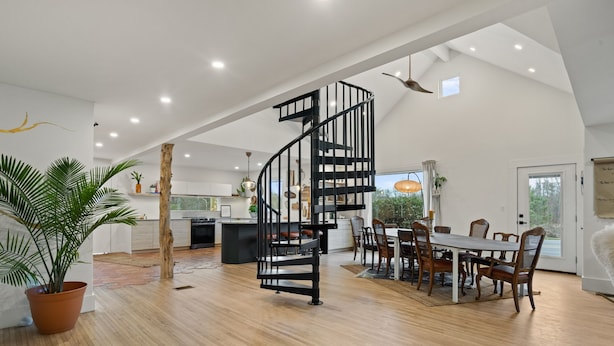 Amplia sala de estar con una escalera espiral negra, piso de madera y un comedor con sillas y una mesa.