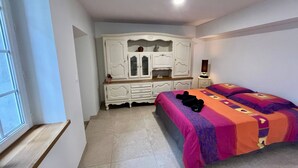 A bedroom with a bed, a white wardrobe, a nightstand, and a window.