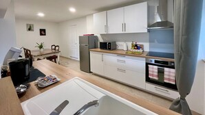 A modern kitchen with white cabinets, a stainless steel refrigerator, a microwave, and an oven. There is a dining table with chairs and a potted plant.