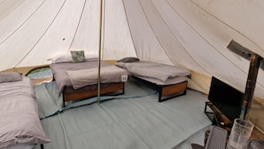 A tent with two beds, a small table, and a sleeping area. - Dog Friendly Cozy Bell Tent With Log Burner (Gaerwen)