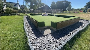 A rectangular garden with a central play area, surrounded by a stone border and grass. - Dog Friendly Cozy Bell Tent With Log Burner (Gaerwen)