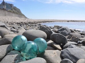 Une plage avec de gros galets lisses et trois sphères de verre posées dessus.