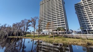 A high-rise building with multiple balconies, a reflection pool, and a grassy area with trees.