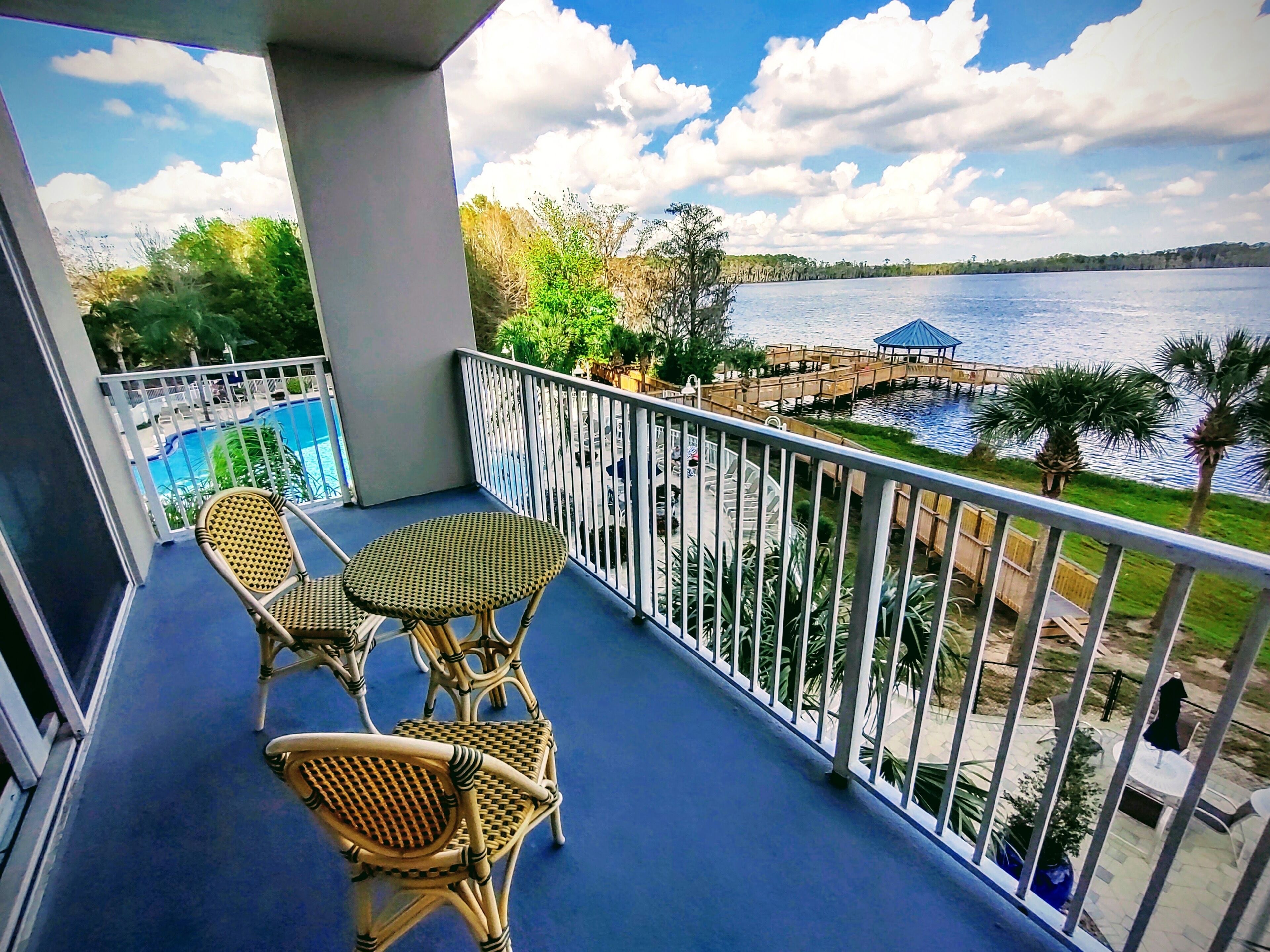 A balcony with wicker furniture, a pool, and a view of a lake with a pier.