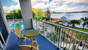 A balcony with wicker furniture, a pool, and a view of a lake with a pier.
