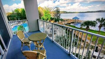 A balcony with wicker furniture, a pool, and a view of a lake with a pier.