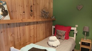 Un dormitorio con cabecera de madera, una cama con almohada blanca y roja, una mesita de noche con lámpara y un estante en la pared con adornos.