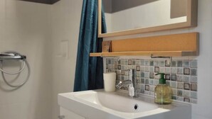 Un baño con lavamanos blanco, espejo, toallero y cortina de ducha.