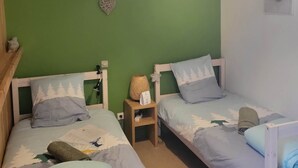 Una habitación con dos camas, una pared verde, una decoración con forma de corazón y una mesita con una lámpara.