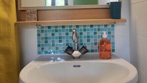 A bathroom with a white sink, a mirror, and a green-tiled wall.