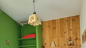 A bedroom with a green wall, wooden panel wall, a bed with a quilt, a desk with a lamp, and a hanging light fixture.