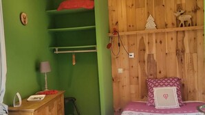 A bedroom with a bed, a dresser, a lamp, and a shelf with decorative items.