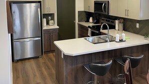 A modern kitchen with a stainless steel refrigerator, a microwave, and a sink. There are wooden cabinets and a white countertop.