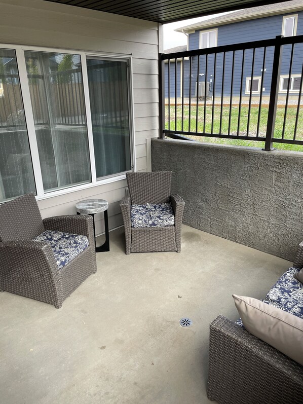 Un patio couvert, aménagé avec des meubles en osier, d’où l’on peut admirer une maison bleue en arrière-plan.