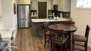 A modern kitchen with a central island, stainless steel appliances, and a dining area with wooden chairs.