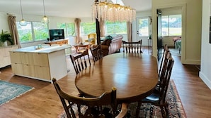 Un comedor amplio con una gran mesa de madera rodeada de sillas, una lámpara de araña y vistas al exterior.