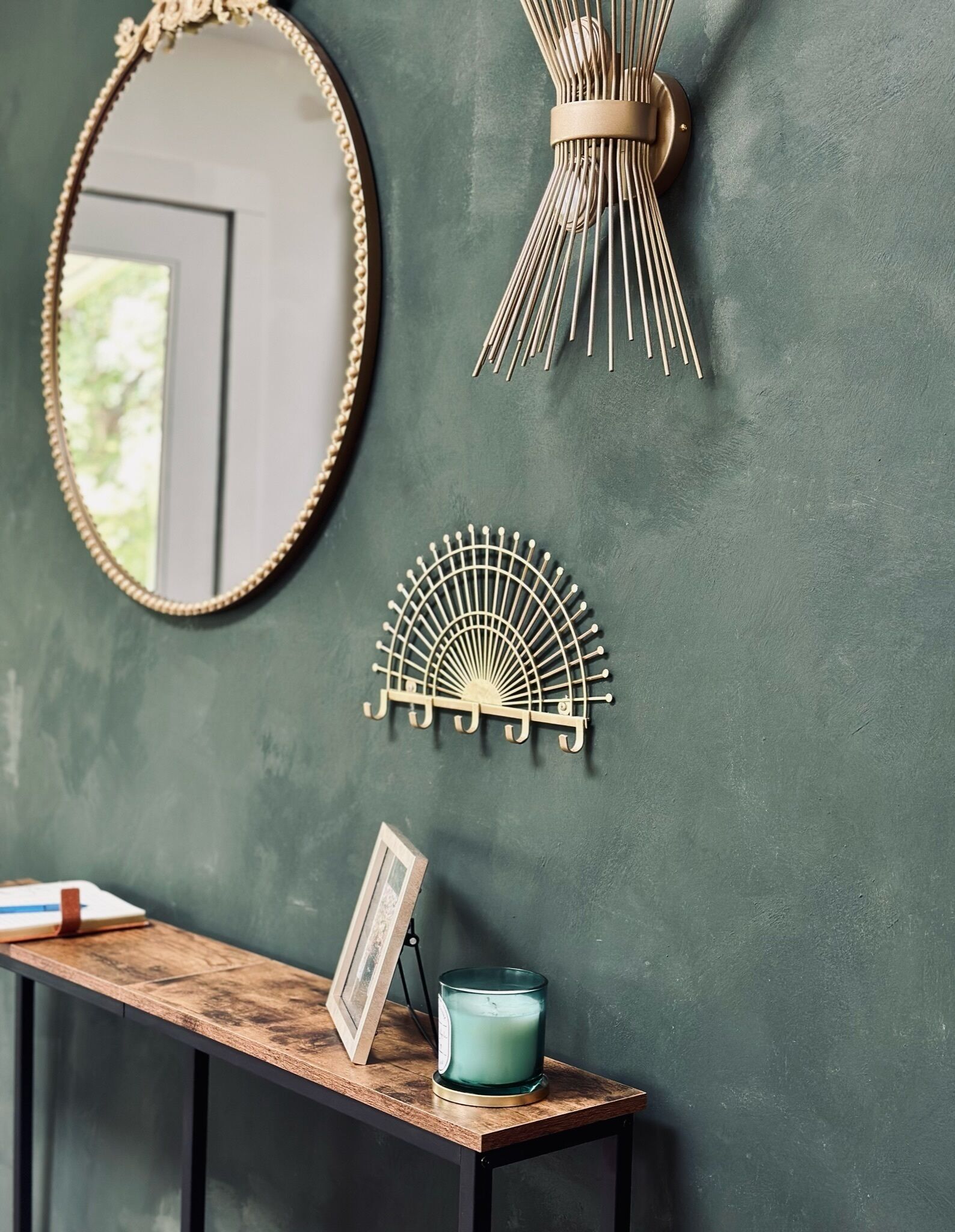 A wall with a mirror, a wall-mounted fan, a wall-mounted light, and a small table with a picture frame and a candle.