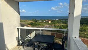 A balcony with a table and chairs, overlooking a coastal landscape with a building in the distance.