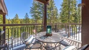 A covered outdoor seating area with metal chairs and a table, overlooking a forested area. - 2 BR/2 BA Condo by Northstar (Truckee)