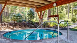 A pool area with a wooden deck, lounge chairs, and a stone wall. - 2 BR/2 BA Condo by Northstar (Truckee)