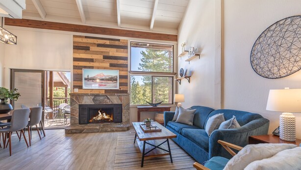 A cozy living room with a fireplace, a blue sofa, and a dining area with chairs and a table. - 2 BR/2 BA Condo by Northstar (Truckee)