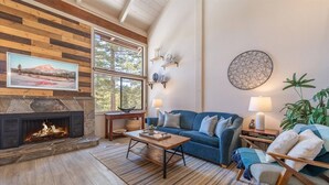 A cozy living room with a fireplace, a blue sofa, a coffee table, and a large window with a mountain view. - 2 BR/2 BA Condo by Northstar (Truckee)