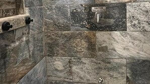 Una dutxa amb un senyal de precaució, rajoles de pedra i un vàter de mà.