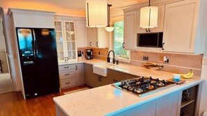 A modern kitchen with a central island, stainless steel appliances, and pendant lighting. - Charming 4-bedroom cottage with AC, WiFi on Little Sebago Lake waterfront (Raymond)