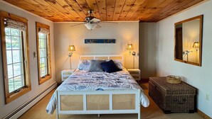 A bedroom with a wooden ceiling, a bed with a white headboard, two bedside lamps, and a large mirror on the wall. - Charming 4-bedroom cottage with AC, WiFi on Little Sebago Lake waterfront (Raymond)