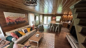 A cozy cabin interior with a wooden ceiling, a sofa with colorful cushions, a dining area, and a kitchen. - Luxury Cabin Hot Tub ATV Trail Cherry Springs (Coudersport)