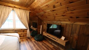 A cozy cabin room with a wooden ceiling, a large window with curtains, a bed, a TV, and bean bags. - Luxury Cabin Hot Tub ATV Trail Cherry Springs (Coudersport)