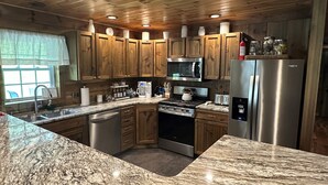 A kitchen with wooden cabinets, a stainless steel refrigerator, a microwave, a stove, and a sink. - Luxury Cabin Hot Tub ATV Trail Cherry Springs (Coudersport)