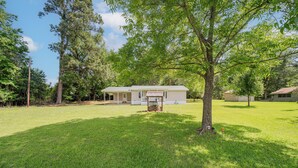 A residential property with a well-maintained lawn, a single-story house with a front porch, and a large tree in the foreground.