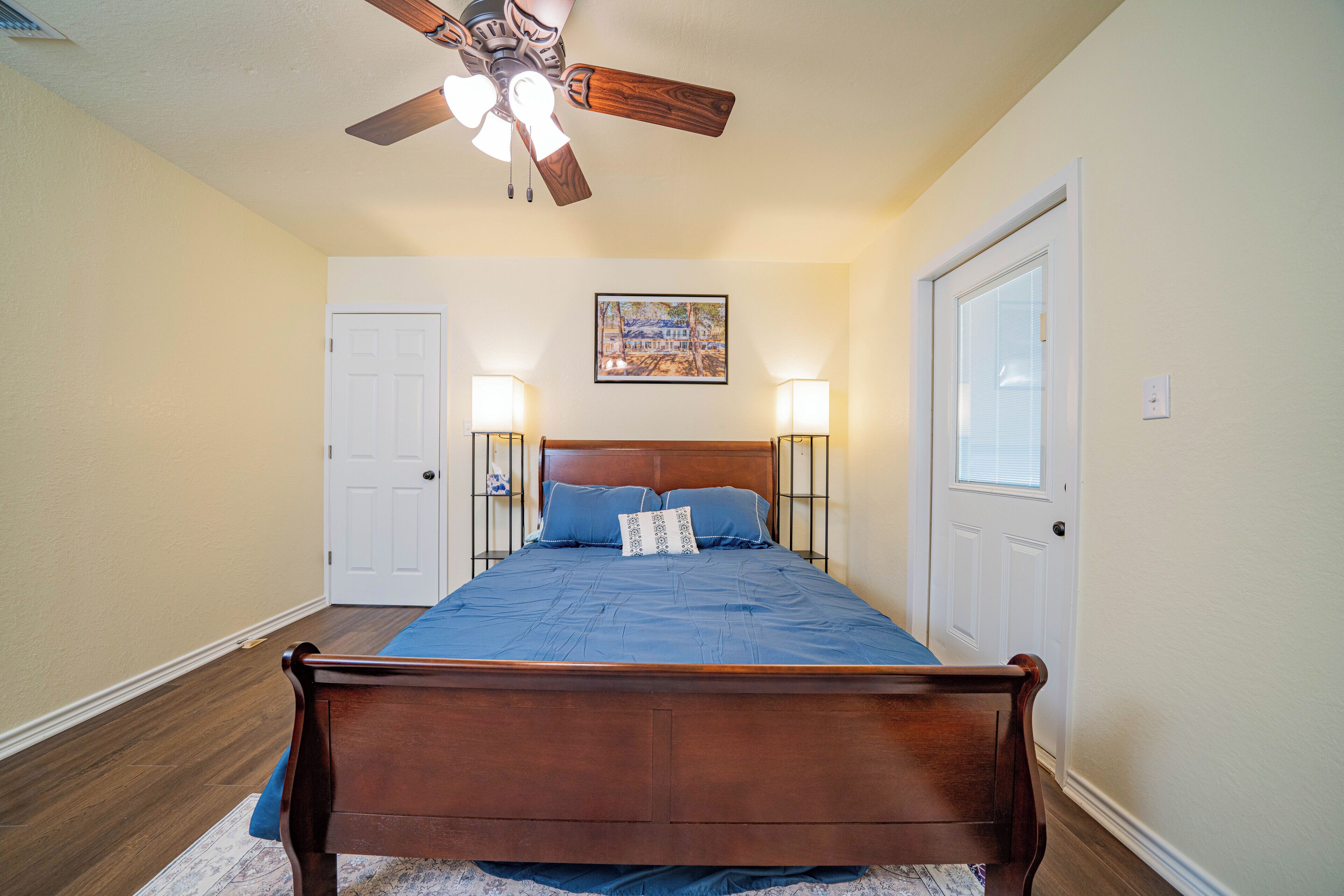 A bedroom with a wooden bed, a ceiling fan, two bedside lamps, and a door with a window.