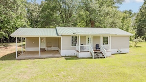 A small, single-story cabin with a porch and a covered porch area, surrounded by trees.
