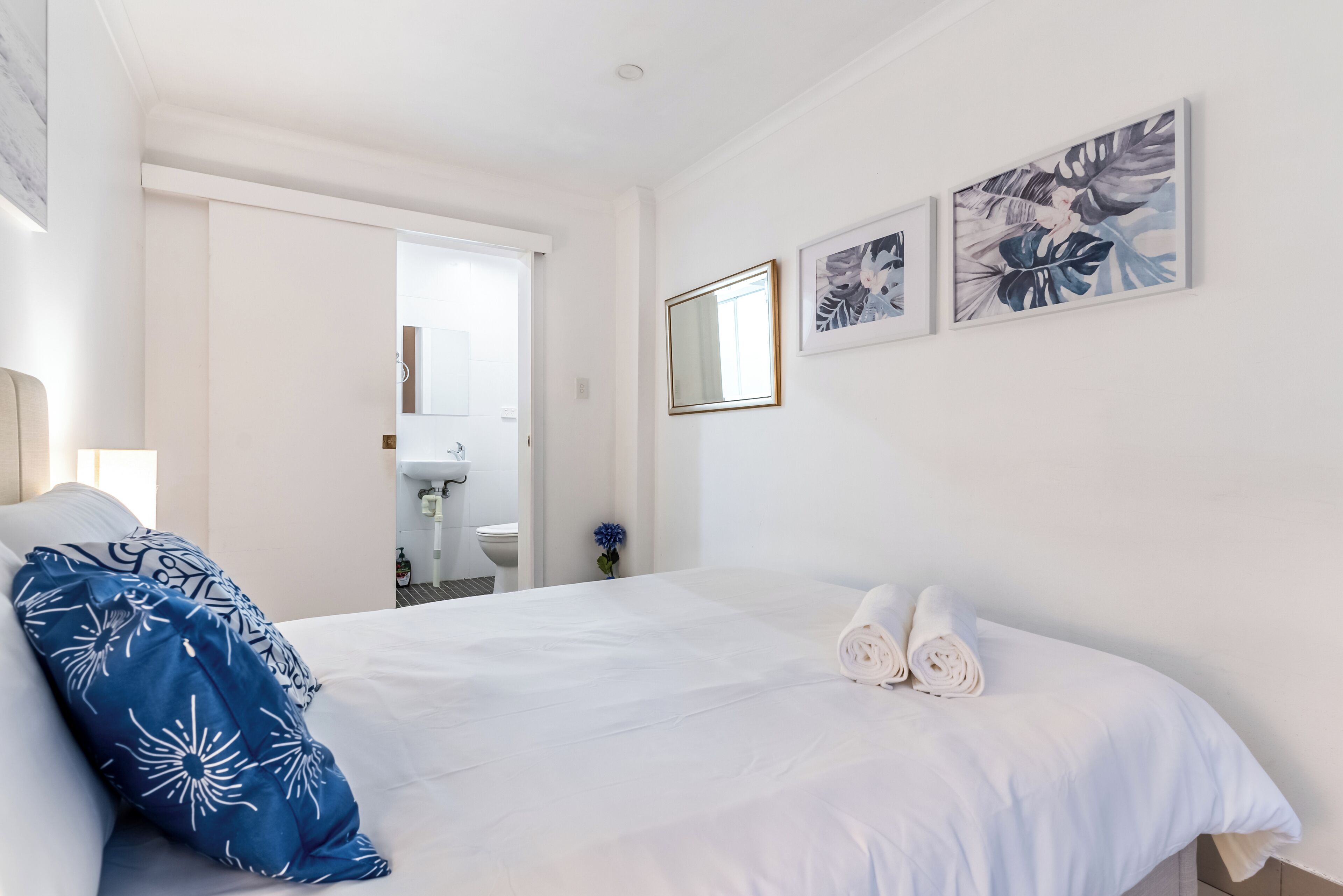 A hotel room with a large bed, a bathroom with a sink, and a mirror on the wall.