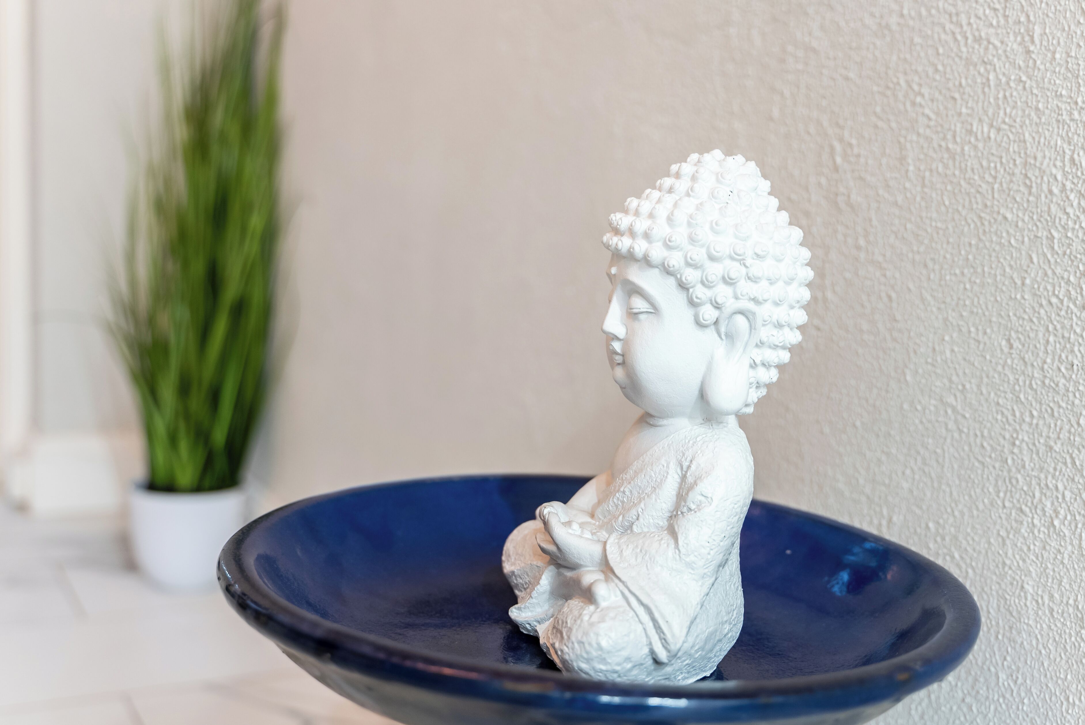 Eine weiße Buddha-Statue sitzt in einer blauen Schale.