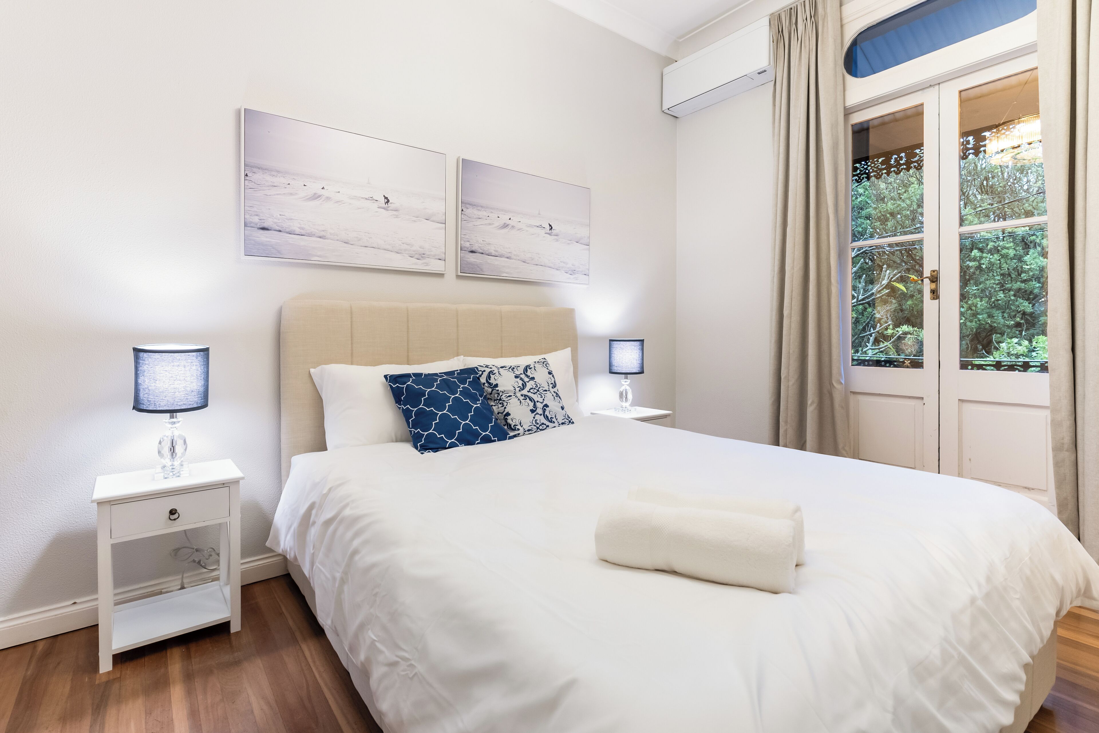 Um quarto bem organizado com uma cama grande, duas mesas de cabeceira, uma janela com cortinas e quadros nas paredes.