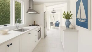 A modern kitchen with white cabinetry, a stainless steel range hood, and a large window with a green textured wall. - The Hamptons Paddington Home (Paddington)