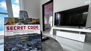 Una sala moderna con un televisor de pantalla plana grande, un mueble blanco para equipo audiovisual y un libro titulado 'Secret Code' sobre un pedestal.